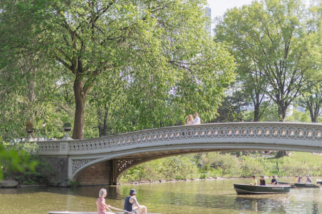 Couple on Bow Bridge during Central Park NYC engagement session with rowboats on the lake below